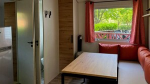 Ein kleines Zimmer mit Holztisch, einer Couch und einem Fenster mit Vorhängen.