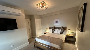Ein Schlafzimmer mit Bett, Nachttischen, einem Wand-Fernseher, einer Deckenleuchte und einer Tür.