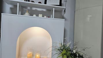 A modern interior with a white fireplace, three lit candles, and a potted plant.