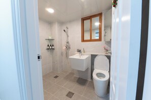 A modern bathroom with a shower, toilet, sink, and a mirror above the sink. - TOV STAY (Pyeongtaek)