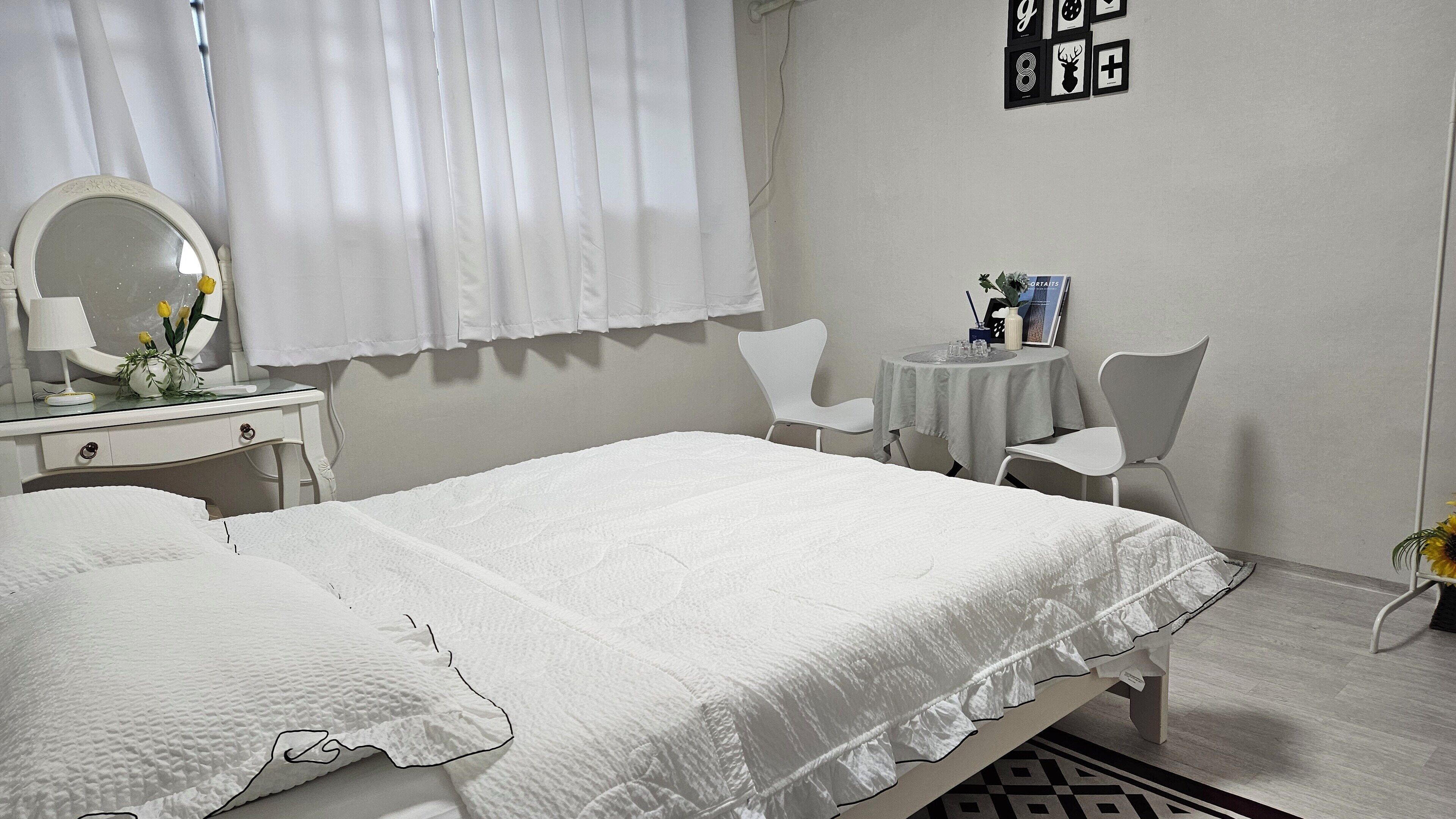 Habitación de hotel con cama, escritorio con espejo, silla, mesita con un florero y un cuadro con marcos.