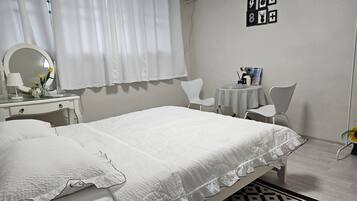 A hotel room with a bed, a desk with a mirror, a chair, a small table with a vase, and a wall with framed pictures.