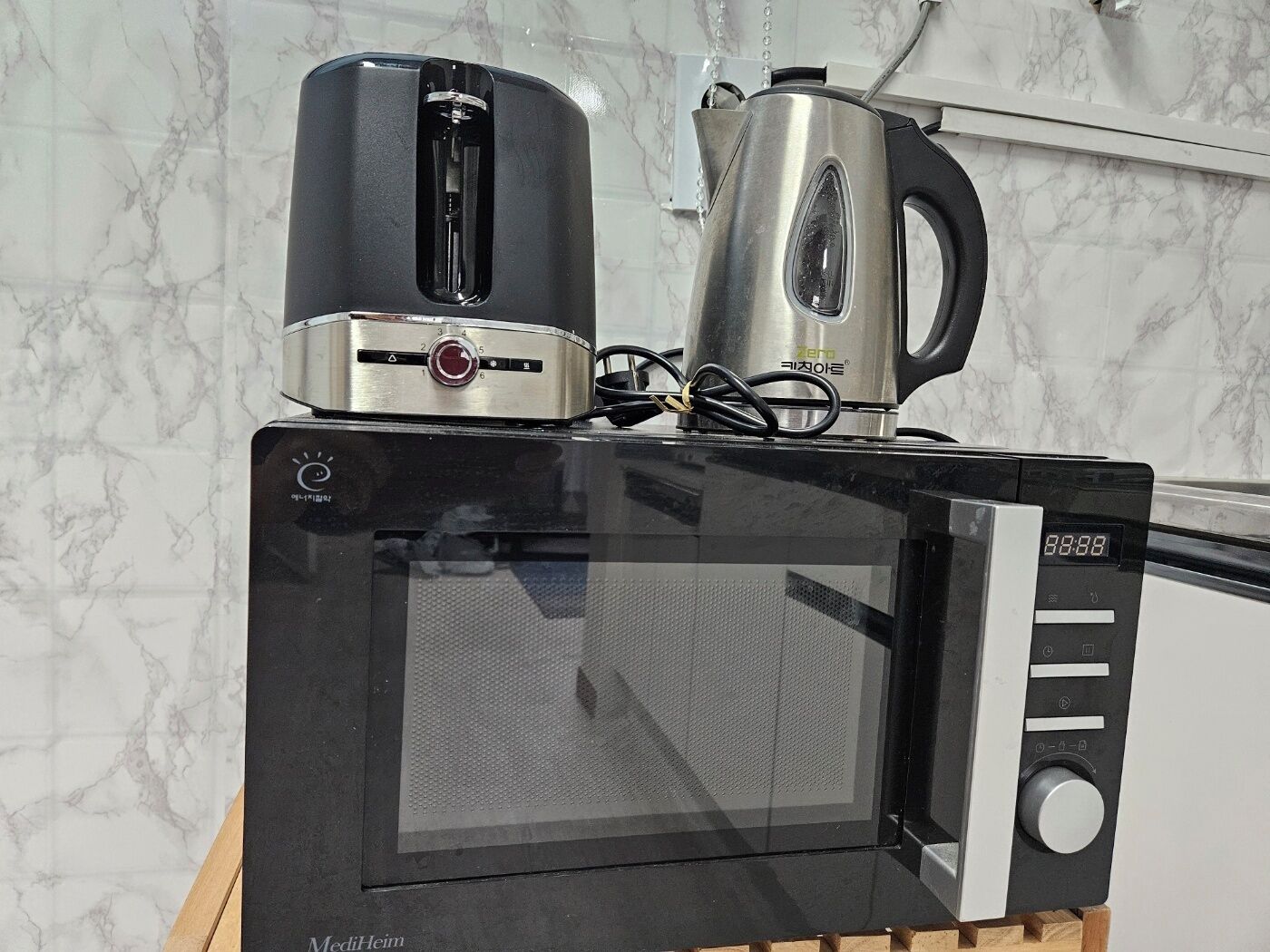 A microwave oven with a digital display, a toaster, and a kettle on top.