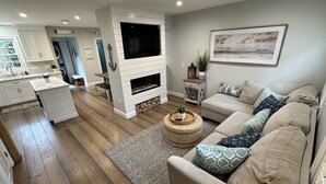 Een moderne woonkamer met een open haard, een zithoek en een keuken op de achtergrond.