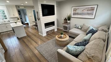 A modern living room with a fireplace, a sofa set, and a kitchen area in the background.