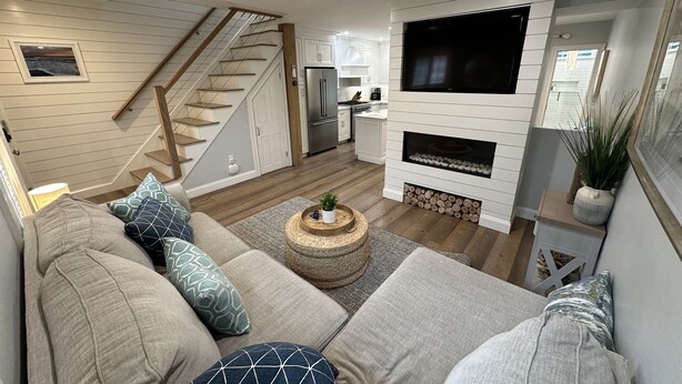 Een moderne woonkamer met een zithoek, een open haard, een televisie en een keuken op de achtergrond.