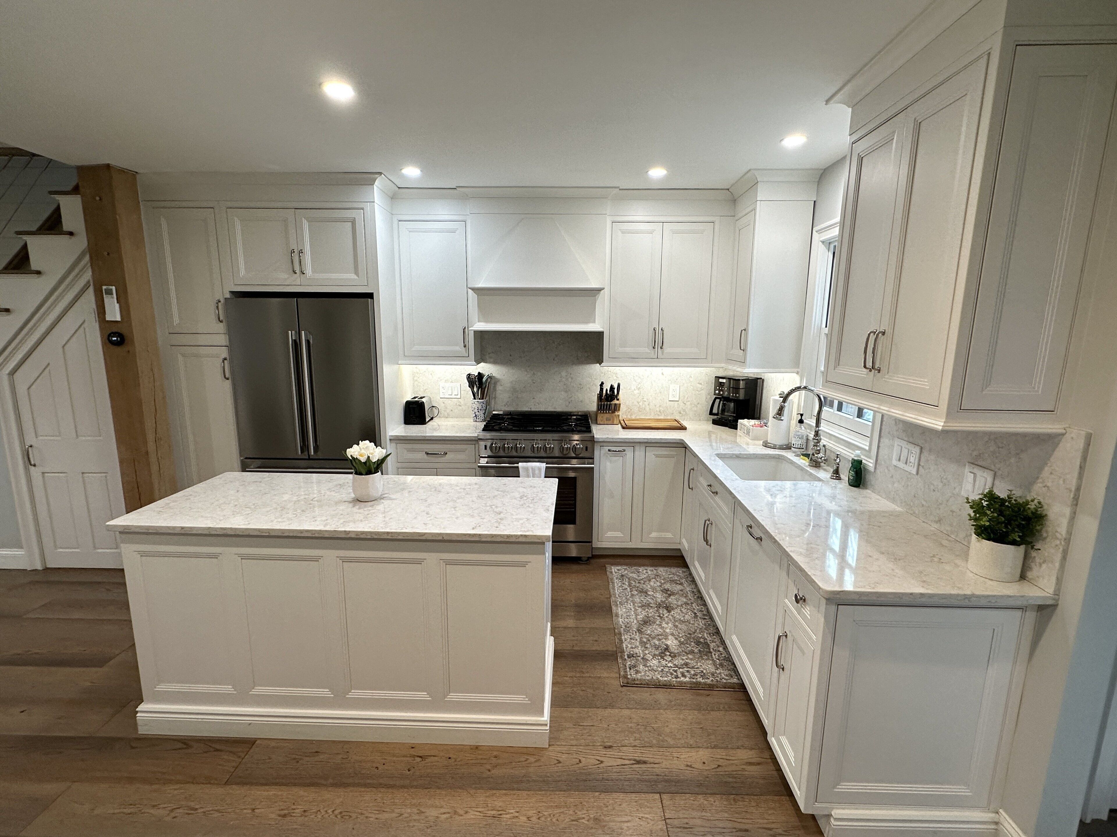 A modern kitchen with white cabinetry, stainless steel appliances, and a marble countertop.