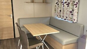 Ein kleiner Raum mit Holztisch und zwei Stühlen, einer Bank und einem Fenster mit blumigen Vorhängen.