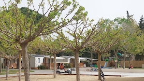 A park with trees, a playground, and a row of mobile homes. - 31m² Mobile Home with Terrace - 3 Bedrooms, Sleeps 6 (La Grande-Motte)