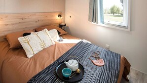 Quarto arrumado com cama, mesa de cabeceira e janela com cortinas.