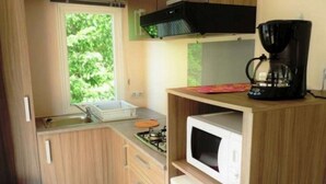 Kompakti keittiö, jossa on kaasuliesi, mikroaaltouuni, kahvinkeitin ja ikkuna, josta avautuu näkymä vehreään maisemaan.