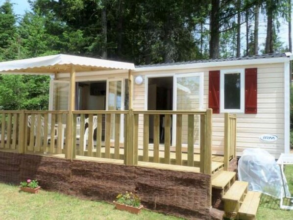 Uma casa móvel com varanda coberta, deck de madeira e um pequeno jardim.
