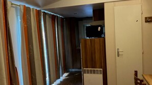 Un couloir étroit avec une armoire en bois, une porte blanche et une petite table entourée de chaises.