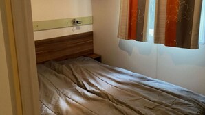 Une petite chambre avec un lit simple, une tête de lit en bois, une table de chevet et une fenêtre avec des rideaux.