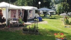 Un camping con tiendas de campaña y vehículos recreativos, un área de césped con plantas en macetas y una persona sentada en una silla.