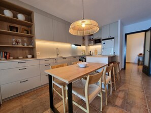 A modern kitchen with white cabinets, a wooden dining table, and a hanging light fixture. - Modern apartment with terrace and pool 50m from the beach (L'Escala)