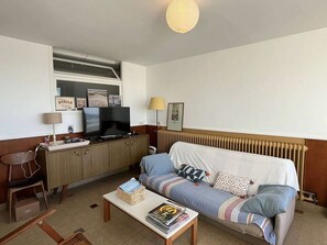 Ein gemütlicher Wohnbereich mit Sofa, kleinem Tisch, Fernseher und Heizkörper.