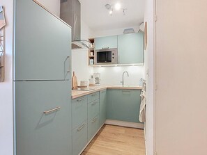 Eine kompakte Küche mit türkis-blauen Schränken, einer Mikrowelle, einem Spülbecken und einer Holz Arbeitsplatte.