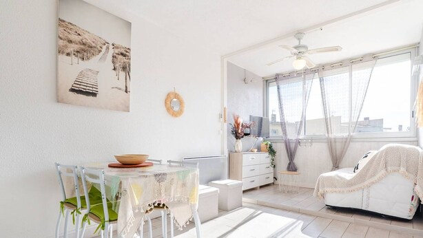 Um quarto claro e ensolarado com uma mesa de jantar, cadeiras, um sofá e um ventilador de teto.