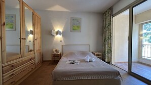 Ein Schlafzimmer mit einem Bett, einem Holzschrank, einem Nachttisch, einer Wandleuchte und einem großen Fenster.