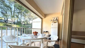 Ein Balkon mit Tisch und Stühlen, einem Kühlschrank und einem Fenster mit Blick auf Bäume und parkende Autos.