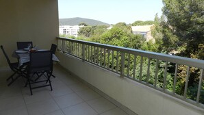 Ein Balkon mit Esstisch und Stühlen, einem weißen Geländer und Blick auf Bäume und Gebäude.