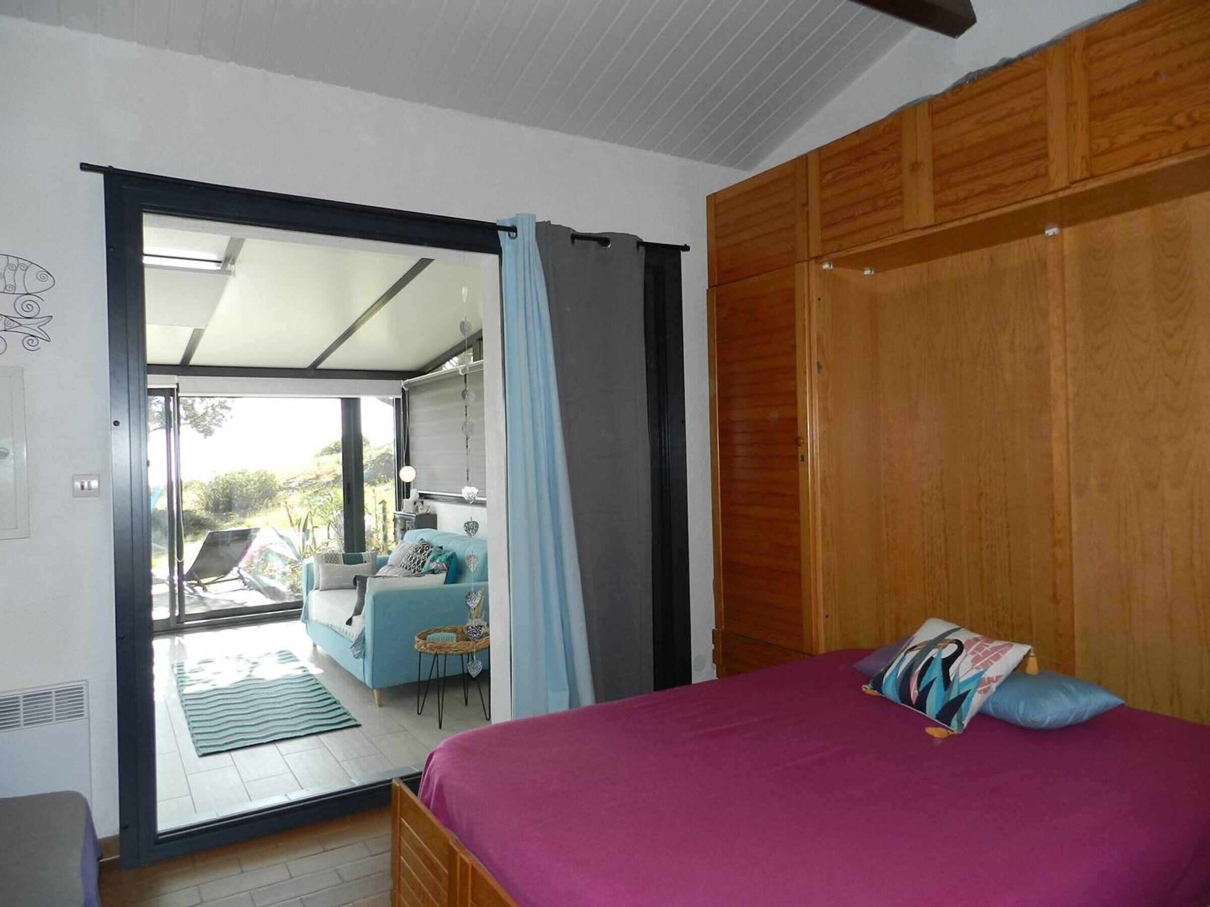 A bedroom with a bed, a wooden wardrobe, and a sliding glass door leading to a balcony.