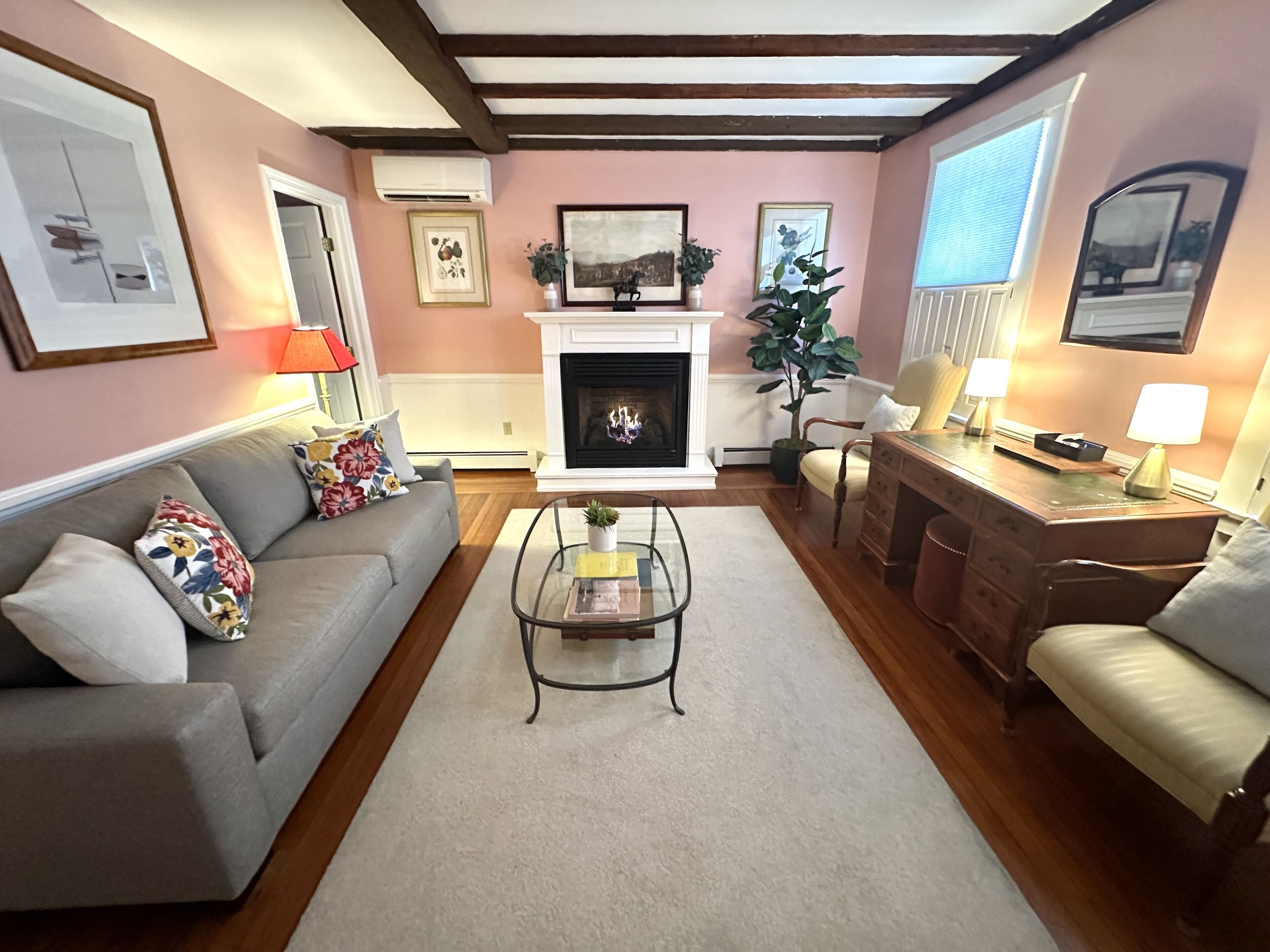 A living room with a fireplace, a sofa, a coffee table, and a desk with a lamp.