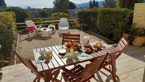 An outdoor patio with a wooden table set for breakfast, surrounded by chairs. - 2 Bedroom Apartment, Air Conditioning, Parking, Sleeps 4 (Bormes-les-Mimosas)