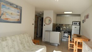 A compact living space with a sofa, a small kitchen area, and a dining table. - 2 Bedroom Apartment, Air Conditioning, Parking, Sleeps 4 (Bormes-les-Mimosas)