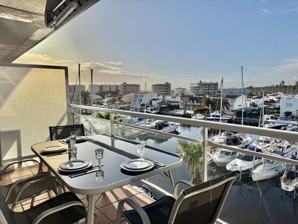 Un comedor con una mesa preparada para dos, con vista a un puerto deportivo con barcos y edificios.