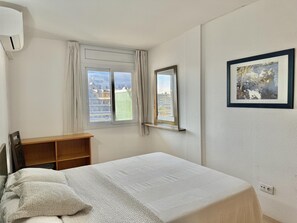 Un dormitorio con una cama, una ventana con cortinas, un estante de madera y un cuadro en la pared.