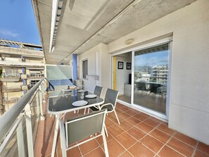 Un balcón con una mesa para dos, una silla y un ventanal corredera que da a una terraza.