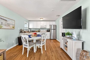 A compact kitchen with white cabinets, a stainless steel refrigerator, and a dining area with white chairs and a table set for two.