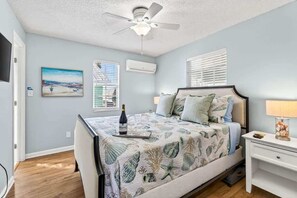 A bedroom with a bed, a ceiling fan, a nightstand, a lamp, and a painting on the wall.
