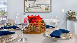 A dining table set with clear glassware, a wicker basket with flowers, and a framed picture on the wall. - Sunny Isles Beach Cottage, Indian Shores! (Indian Shores)