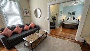 A living room with a dark grey sofa, a wooden coffee table, and a grey carpet. - Exposed Brick Suite 1 Bed/ 1 Bath/ Pullout Sofa 1 Bedroom Apts (Newport)