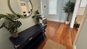 A room with a dark blue console table, a large mirror, and two potted plants. - Exposed Brick Suite 1 Bed/ 1 Bath/ Pullout Sofa 1 Bedroom Apts (Newport)