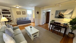 A living room with a sofa, coffee table, and a dining area with a table and chairs. There is a bookshelf and a star decoration on the wall. - Spacious Three Room Suite Downtown Newport #16 1 Bedroom Home (Newport)