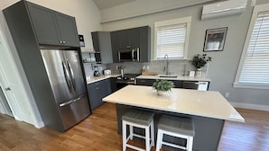 A modern kitchen with grey cabinets, stainless steel appliances, a central island with stools, and a window with blinds. - Brand New Construction! 2bed/1bath W/private Deck - Unit 2 2 Bedroom Apts (Newport)