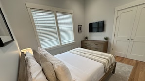 A bedroom with a bed, a dresser, a TV, and a window with blinds. - Brand New Construction! 2bed/1bath W/private Deck - Unit 2 2 Bedroom Apts (Newport)