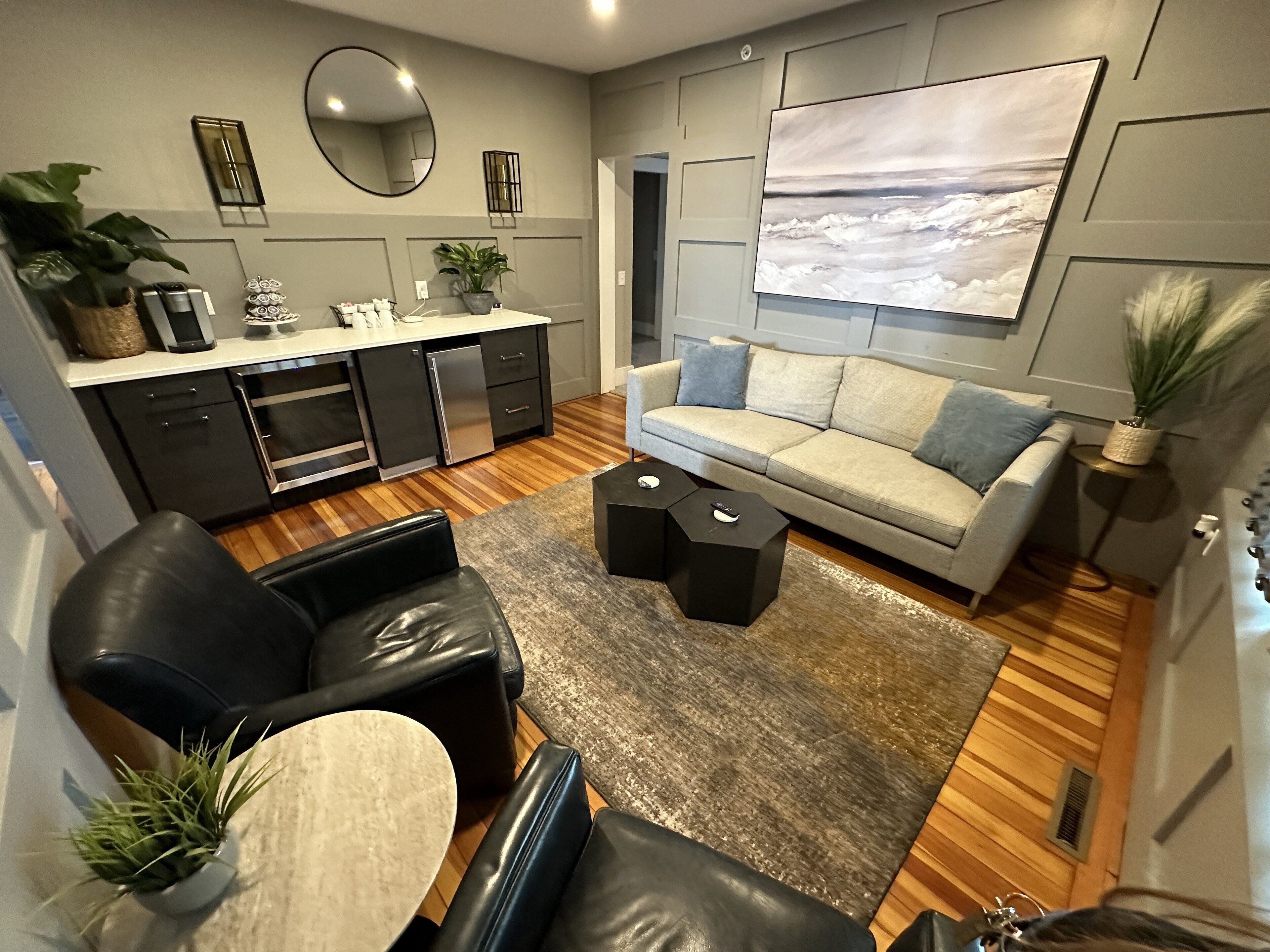 A modern living room with a sofa, coffee table, and chairs. There is a kitchen area with a refrigerator and a dining table.