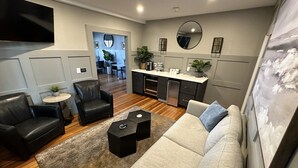A modern living room with a sofa, armchairs, a coffee table, and a kitchen area with a refrigerator and cabinets. - Bright 1 Bed/1 Bath On Historic Pelham St - Unit 2 1 Bedroom Home (Newport)