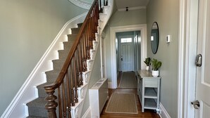A staircase with a wooden handrail and white balusters, leading to a landing with a white radiator and a small table with a plant. - Spacious Suite 1 Bed/ 1 Bath/ Pullouts Sofas - Unit 5 1 Bedroom Apts (Newport)