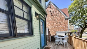 A wooden deck with a blue door, a small outdoor table with chairs, and a brick building in the background. - Downtown Newport 2br Apartment W/ Parking & Deck - Unit 4 2 Bedroom Apts (Newport)