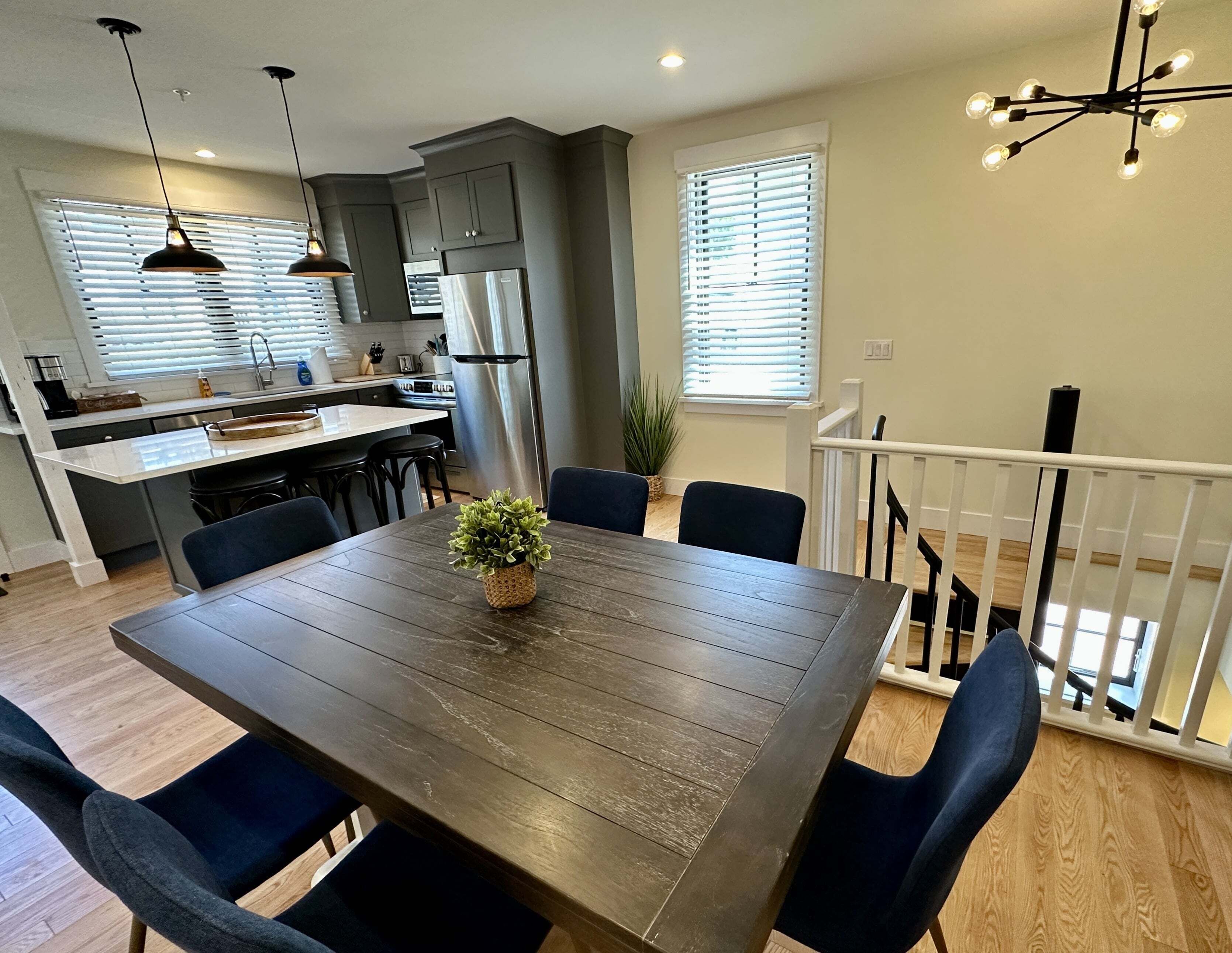 A modern kitchen with a central island, a dining area with a wooden table and chairs, and a staircase leading to an upper level.