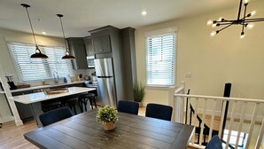 A modern kitchen with a central island, a dining area with a wooden table and chairs, and a staircase leading to an upper level. - Downtown Newport 2br Apartment W/ Parking & Deck - Unit 4 2 Bedroom Apts (Newport)