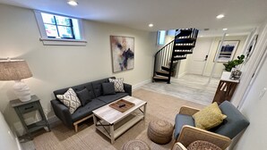 A living room with a sofa, coffee table, and ottoman, a staircase, and a view of the hallway. - Downtown Newport 2br Apartment W/ Parking & Deck - Unit 4 2 Bedroom Apts (Newport)
