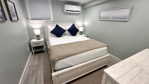 A bedroom with a bed, bedside tables, an air conditioner, a window, and a framed picture on the wall. - Downtown Newport 2br Apartment W/ Parking & Deck - Unit 4 2 Bedroom Apts (Newport)