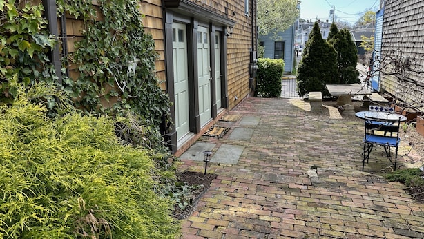 A narrow brick pathway leading to a wooden house with a green door, surrounded by greenery and a small garden area with a table and chairs. - Unique 2 Bed 1 Bath Apartment Off Broadway #3 2 Bedroom Apts (Newport)
